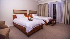 A hotel room with a double bed, two bedside tables, a small wooden bench, and a large window with curtains. - Adelante Lodge (Bloemfontein)