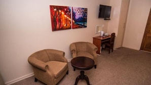 A living room with two armchairs, a coffee table, and a flat-screen TV mounted on the wall. - Adelante Lodge (Bloemfontein)