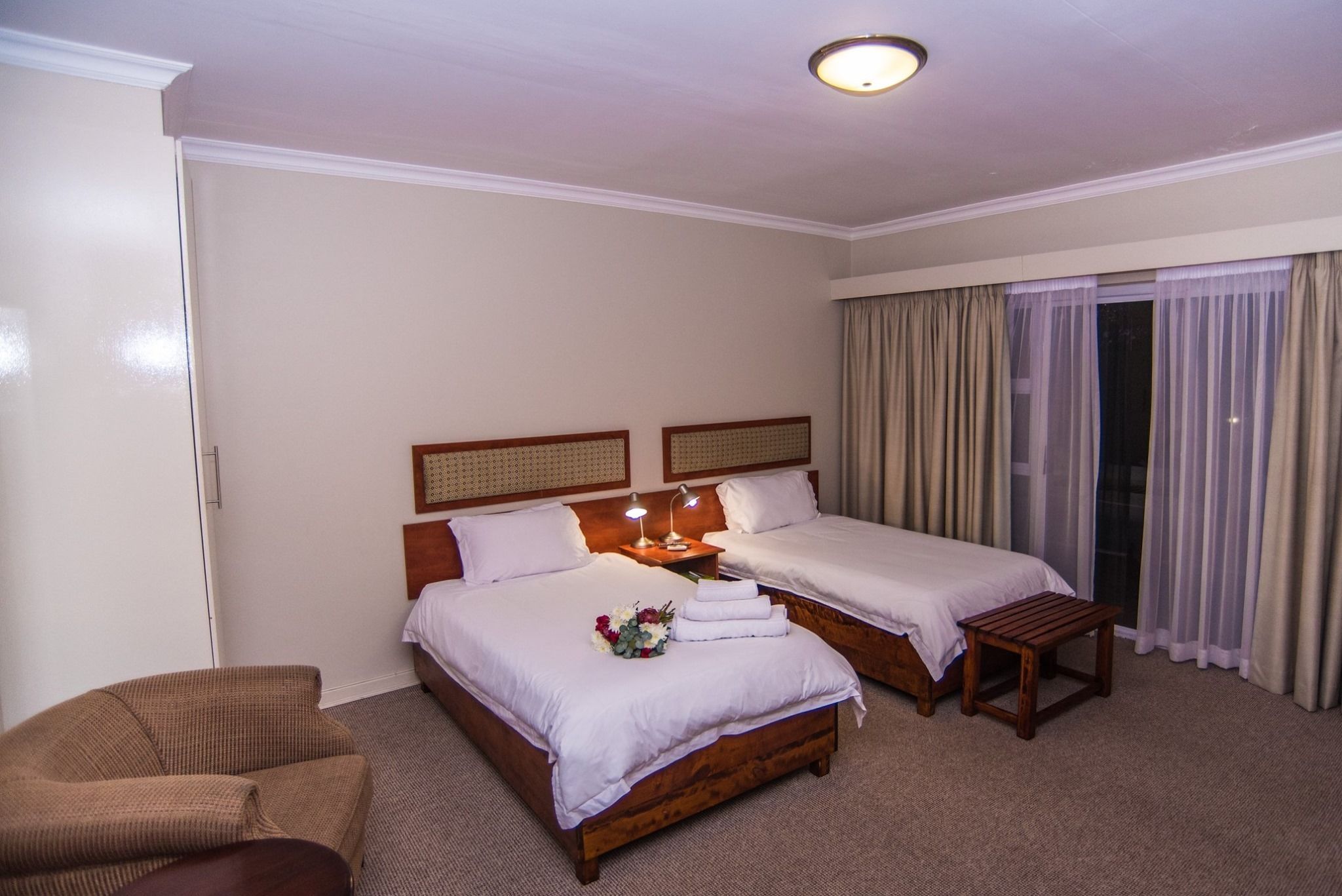 A hotel room with two beds, a wooden headboard, a small wooden table, and a couch.