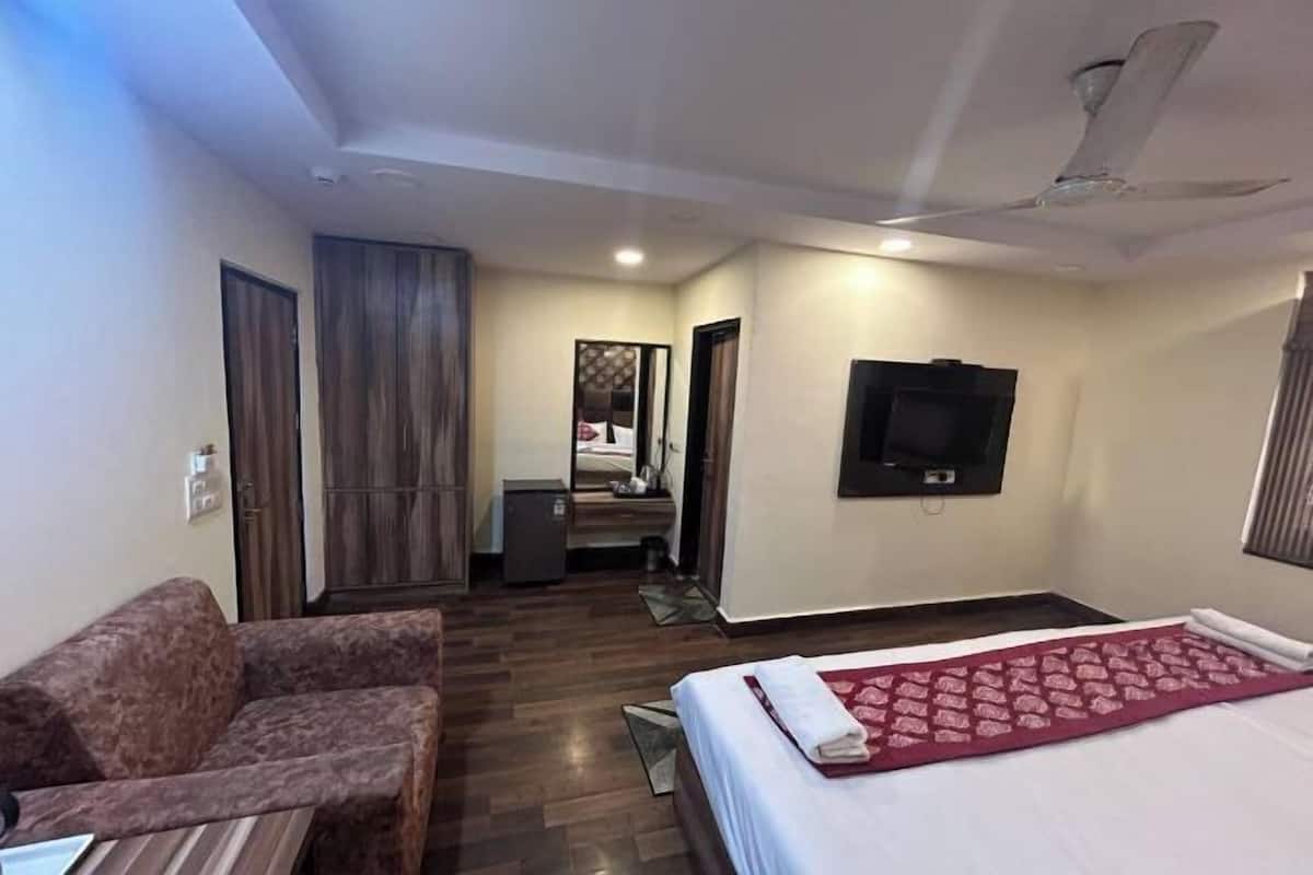 A hotel room with a bed, a sofa, a television, and a ceiling fan.