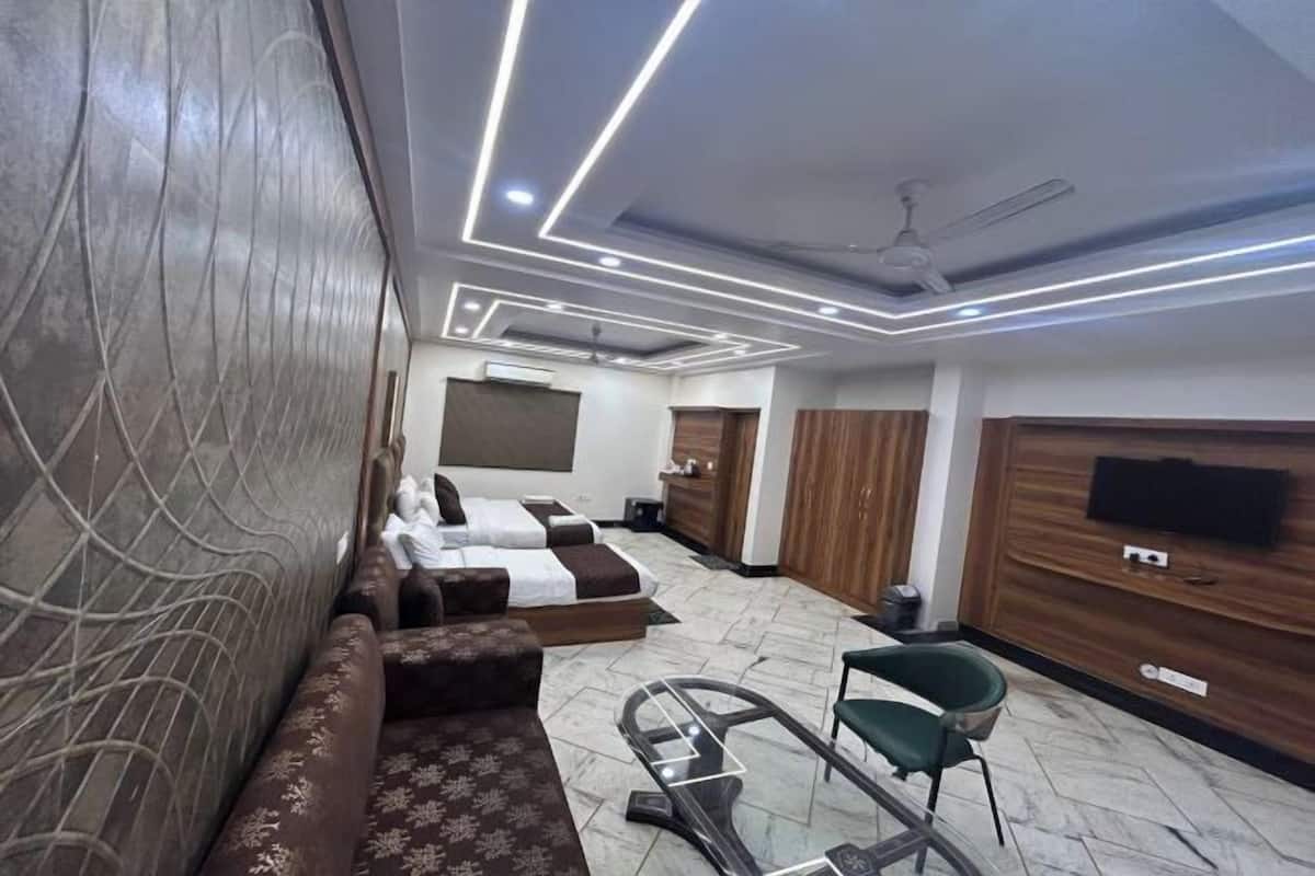 A hotel room with a sofa, a glass table, a chair, a bed, a TV, and a ceiling fan.