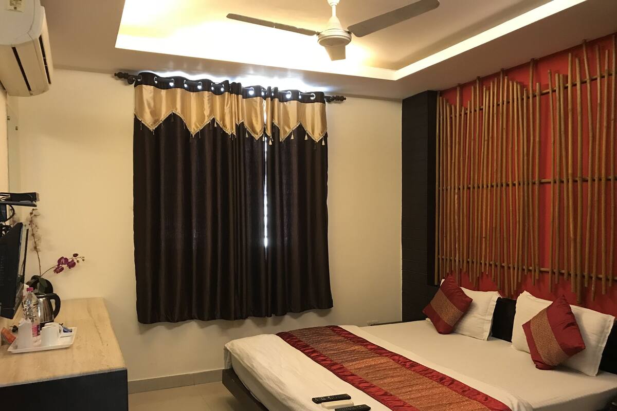 Habitación de hotel con cama, escritorio, cafetera y ventana con cortinas.