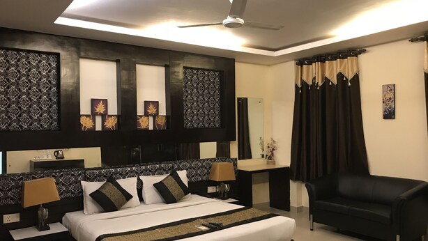 Una habitación de hotel moderna con una cama grande, un sillón negro, un ventilador de techo y paneles decorativos en la pared.