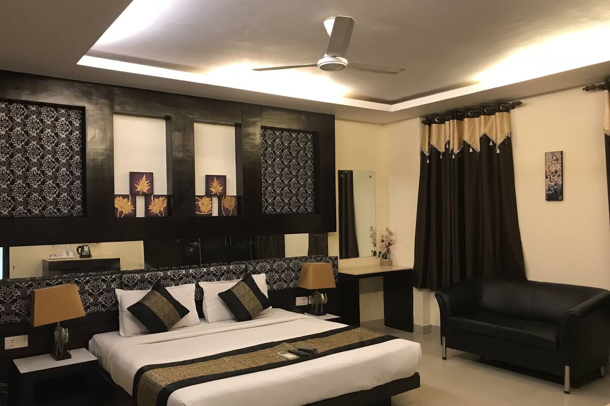 Una habitación de hotel moderna con una cama grande, un sillón negro, un ventilador de techo y paneles decorativos en la pared.
