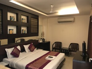 Habitación de hotel con una cama, un escritorio, dos sillas, una televisión y obras de arte en las paredes.