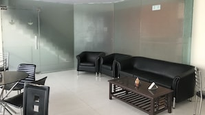 Un área de espera moderna con un panel de vidrio, un sofá de cuero negro, una mesa de centro de vidrio y un comedor con sillas y una mesa.