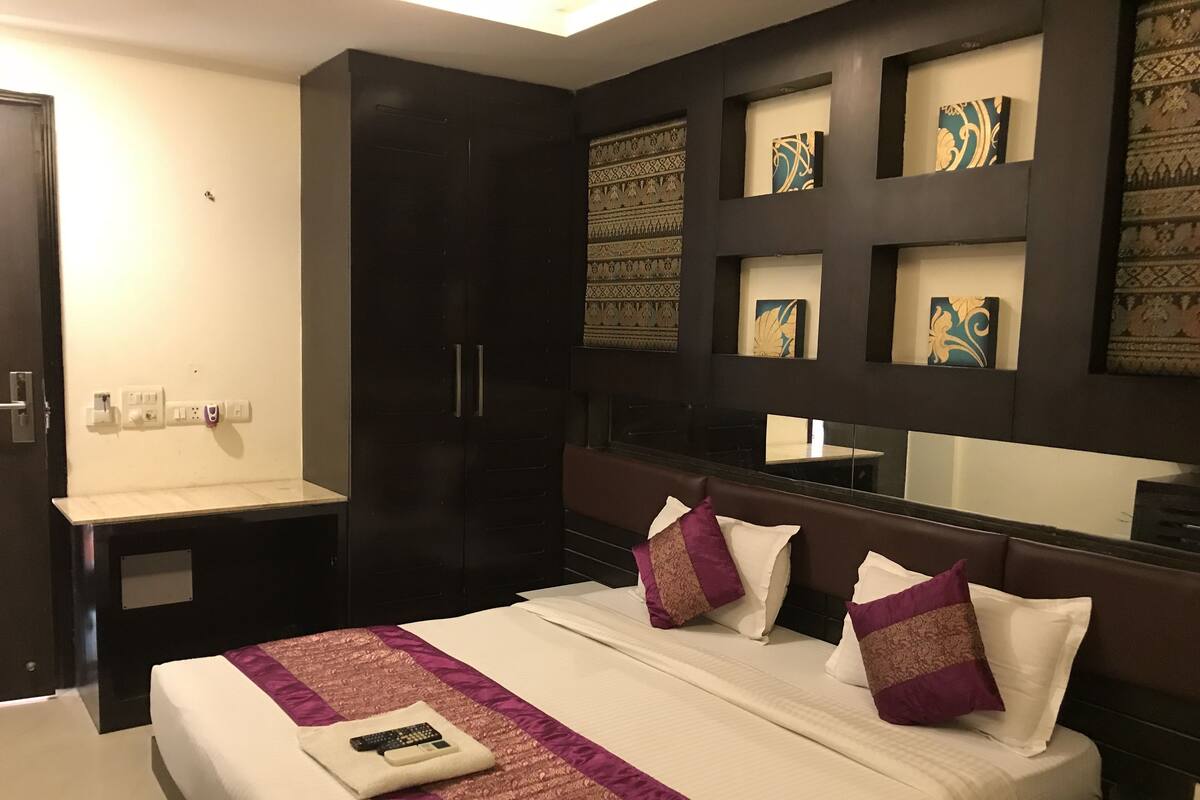 Habitación de hotel con una cama grande, un armario oscuro, un tocador con espejo y una pared con paneles decorativos.