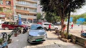 A street view with parked cars, a motorcycle, and a building with multiple floors and balconies. - Hotel Jashn Inn near Apollo Hospital, Delhi (New Delhi)