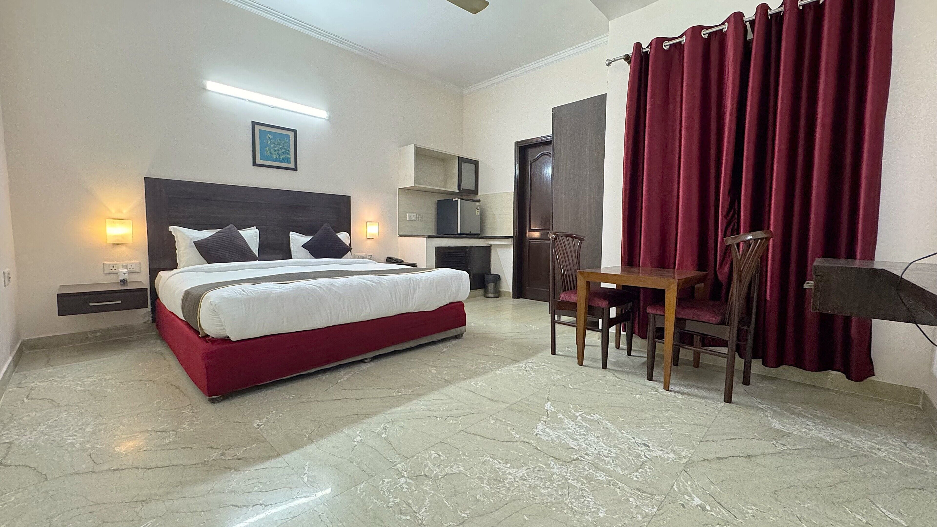 A hotel room with a bed, bedside lamps, a desk with chairs, a microwave, and a red curtain.