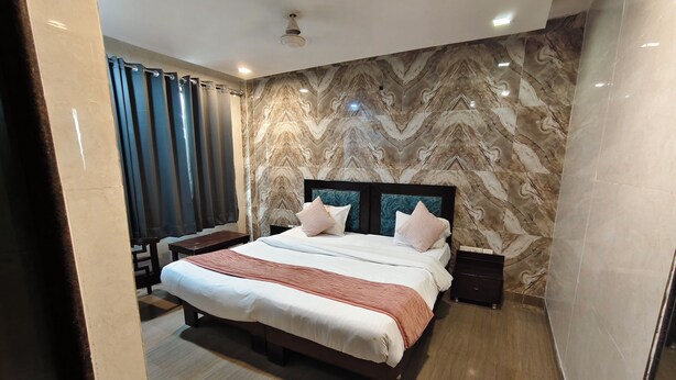 A modern hotel room with a marble-patterned wall, a large bed with a wooden headboard, and a bedside table.