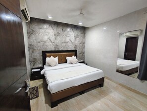 A bedroom with a marble-patterned wall, a wooden bed frame, and a ceiling fan. - The Gera (New Delhi)