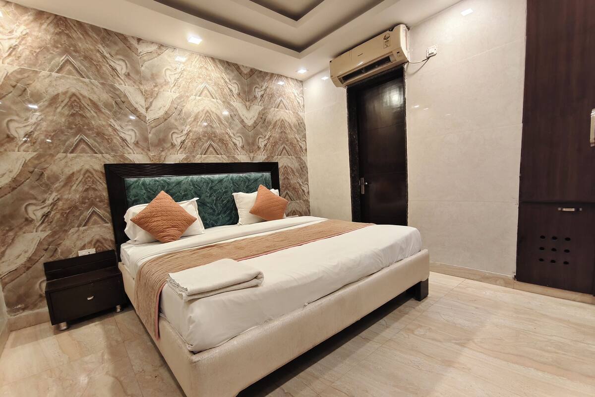 Un dormitorio moderno con una pared con diseño de mármol, una cama grande con cabecera, una puerta oscura y un equipo de aire acondicionado.