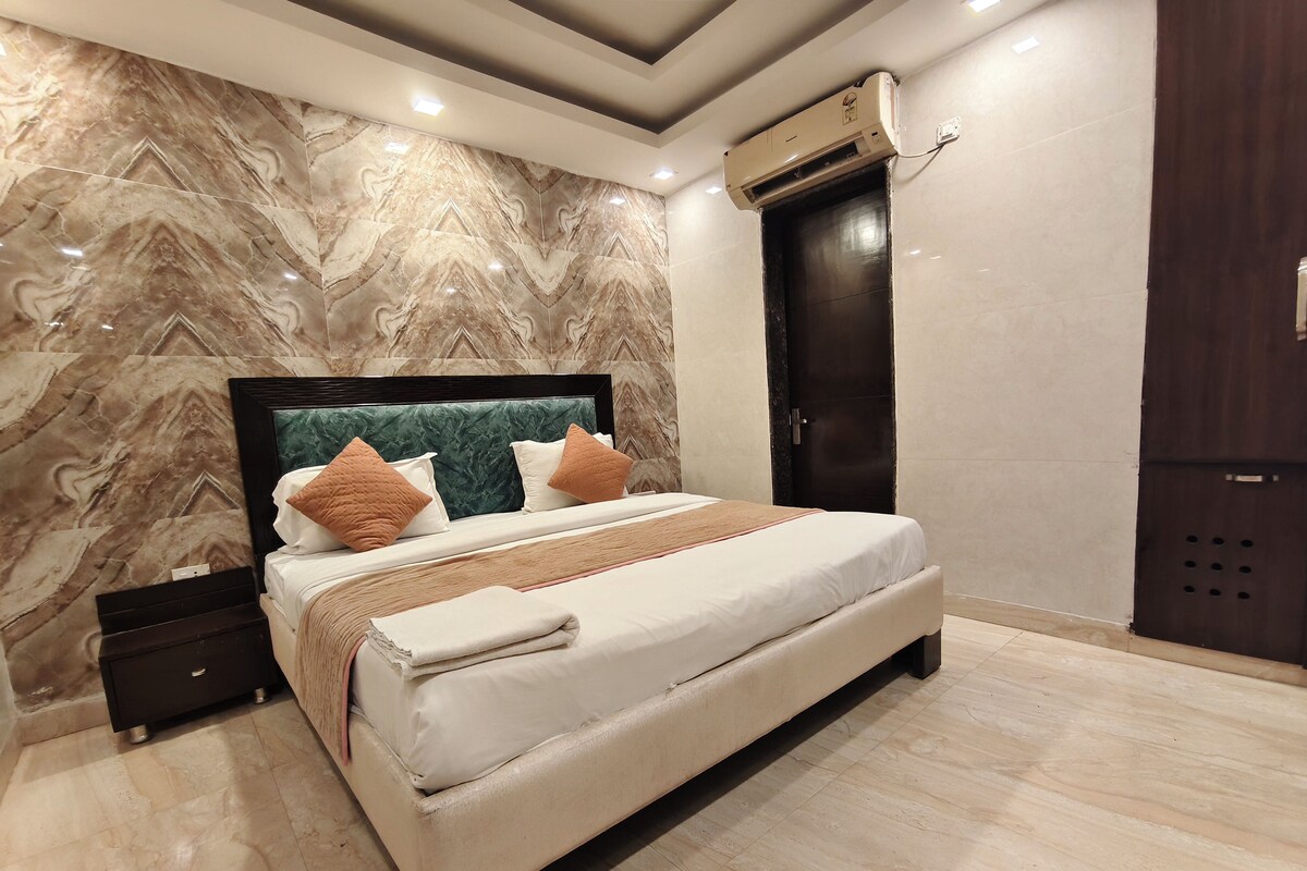 A modern bedroom with a marble-patterned wall, a large bed with a headboard, a dark door, and an air conditioning unit.