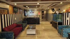 A hotel lobby with striped walls, a reception desk, a reception area, a coffee machine, a TV, a fan, a clock, a fish tank, and seating areas.