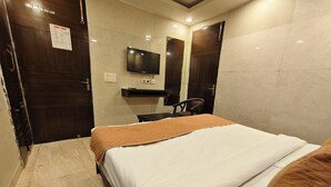 A hotel room with a bed, a television mounted on the wall, a chair, and a wooden door.