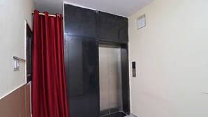 A closed elevator door with a red curtain partially covering it, a light switch, and a small vent on the wall. - Royal Palce (new Delhi)