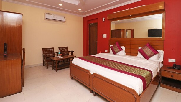 A hotel room with a large bed, a wooden nightstand, a desk with two chairs, a ceiling fan, and a wall-mounted air conditioner. - Royal Palce (new Delhi)