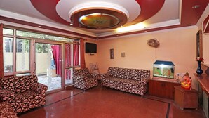 A spacious room with a patterned sofa set, a fish tank, and a television mounted on the wall. - Royal Palce (new Delhi)