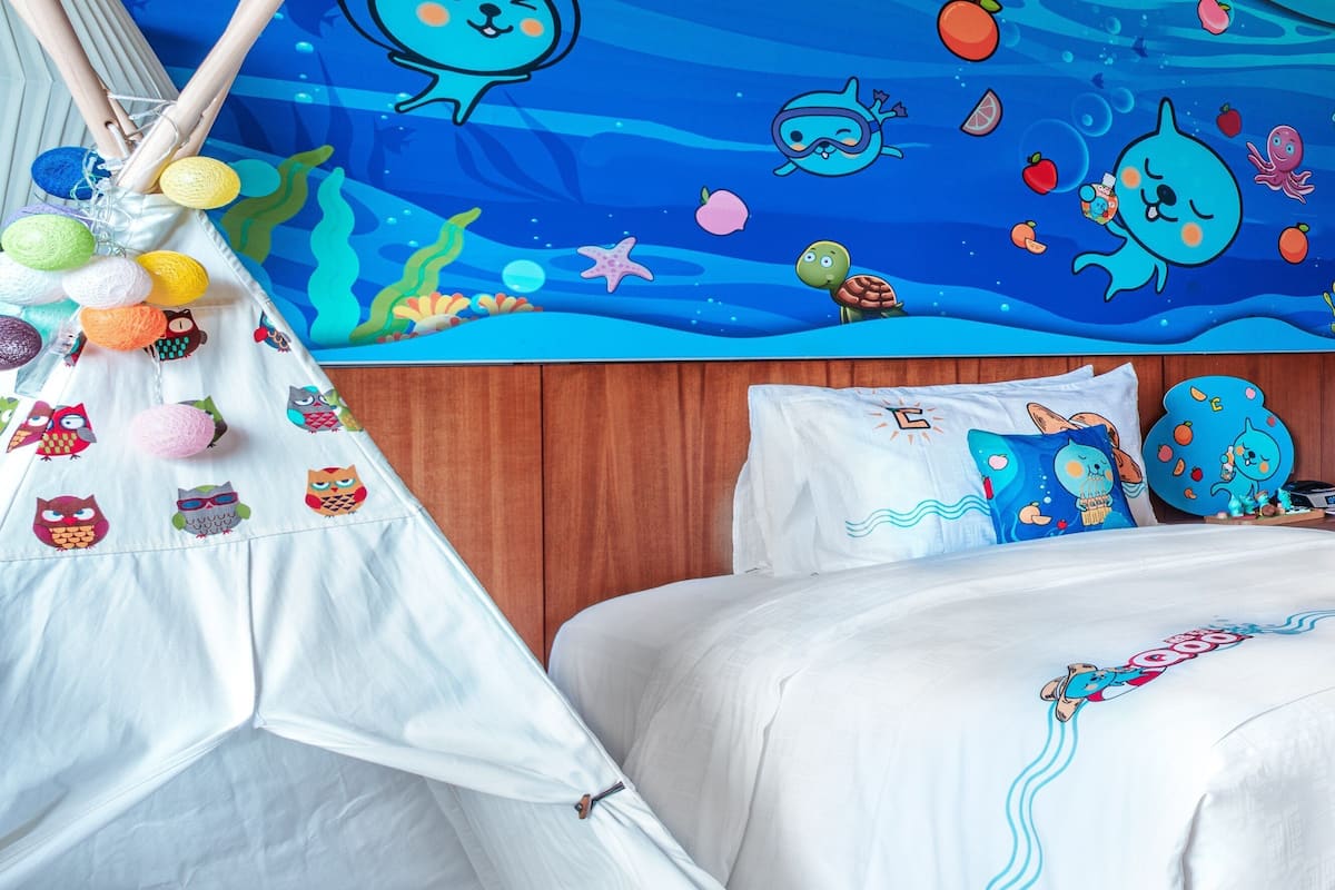 A bedroom with a bed, a white tent with colorful decorations, and a mural with sea creatures.
