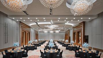 A spacious conference room with round tables, black chairs, and floral centerpieces.