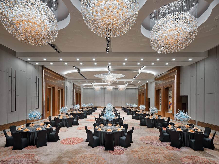 A spacious conference room with round tables, black chairs, and floral centerpieces.