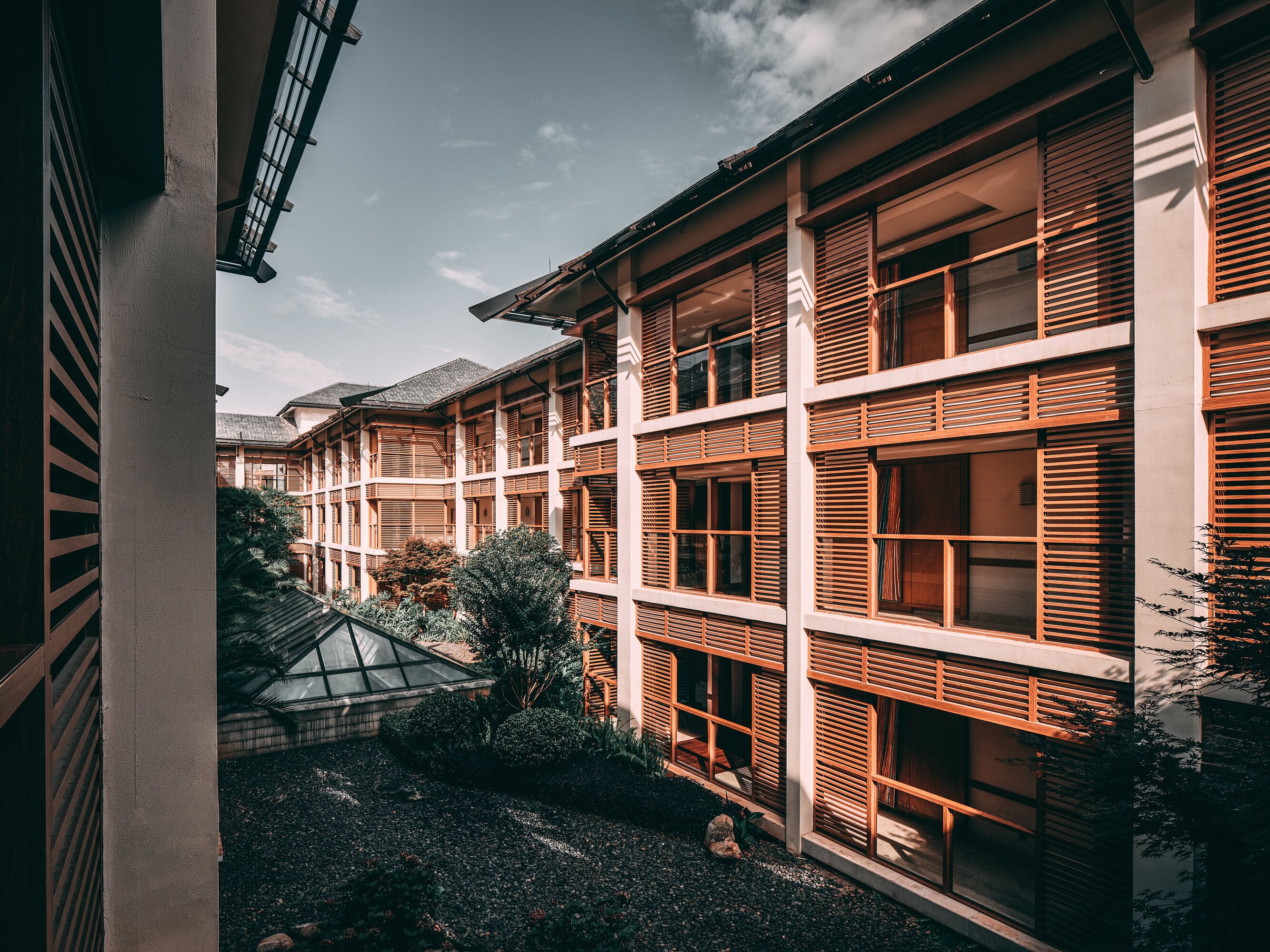 Un edificio de varios pisos con contraventanas de madera, un espacio al aire libre cubierto y un patio de grava.