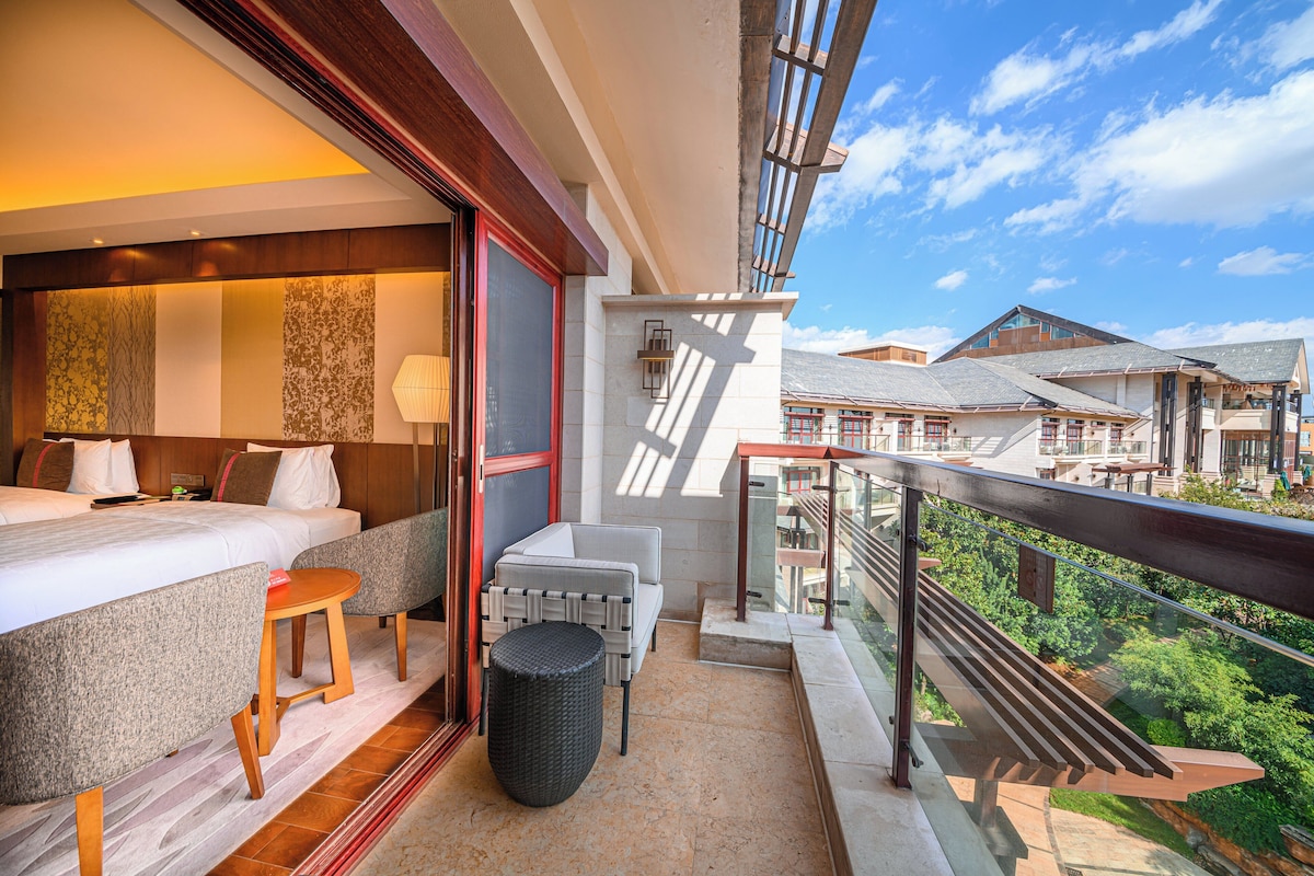 Een hotelkamer met een bed, zithoek en een balkon met uitzicht op een woonwijk.