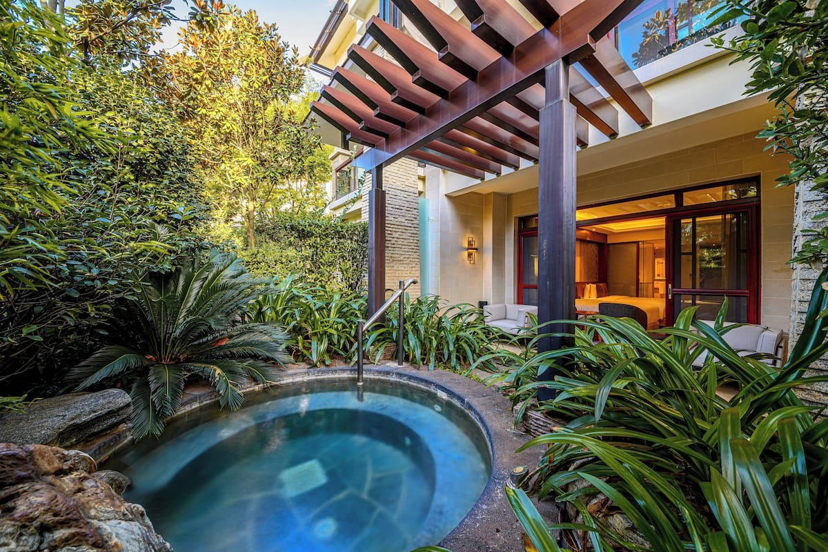 A spa area with a hot tub surrounded by lush greenery and a wooden pergola.
