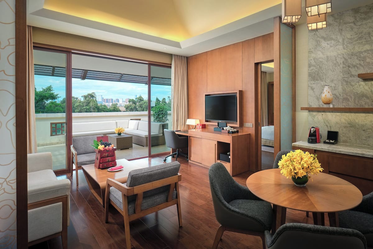 A modern hotel room with a balcony, a sofa, a dining table, and a TV.
