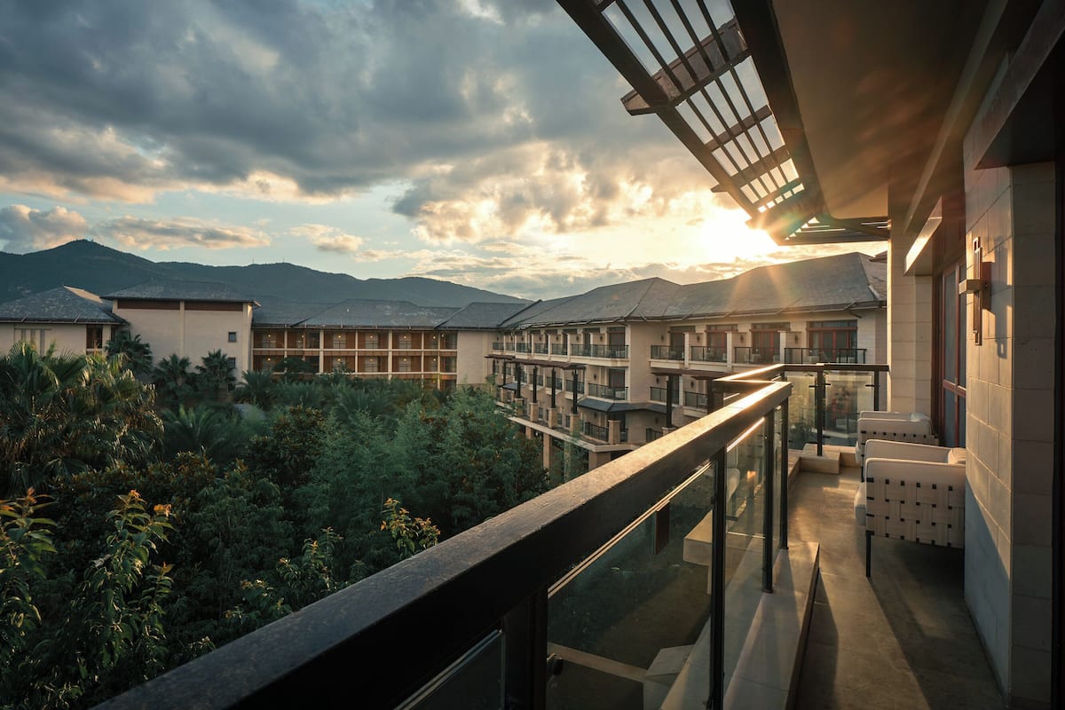 A modern hotel with a balcony overlooking a lush garden and mountains.