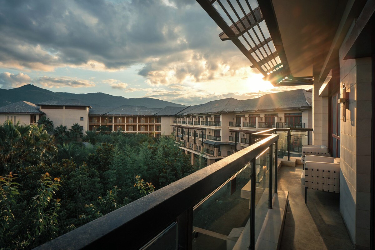Een modern hotel met een balkon dat uitkijkt over een weelderige tuin en bergen.