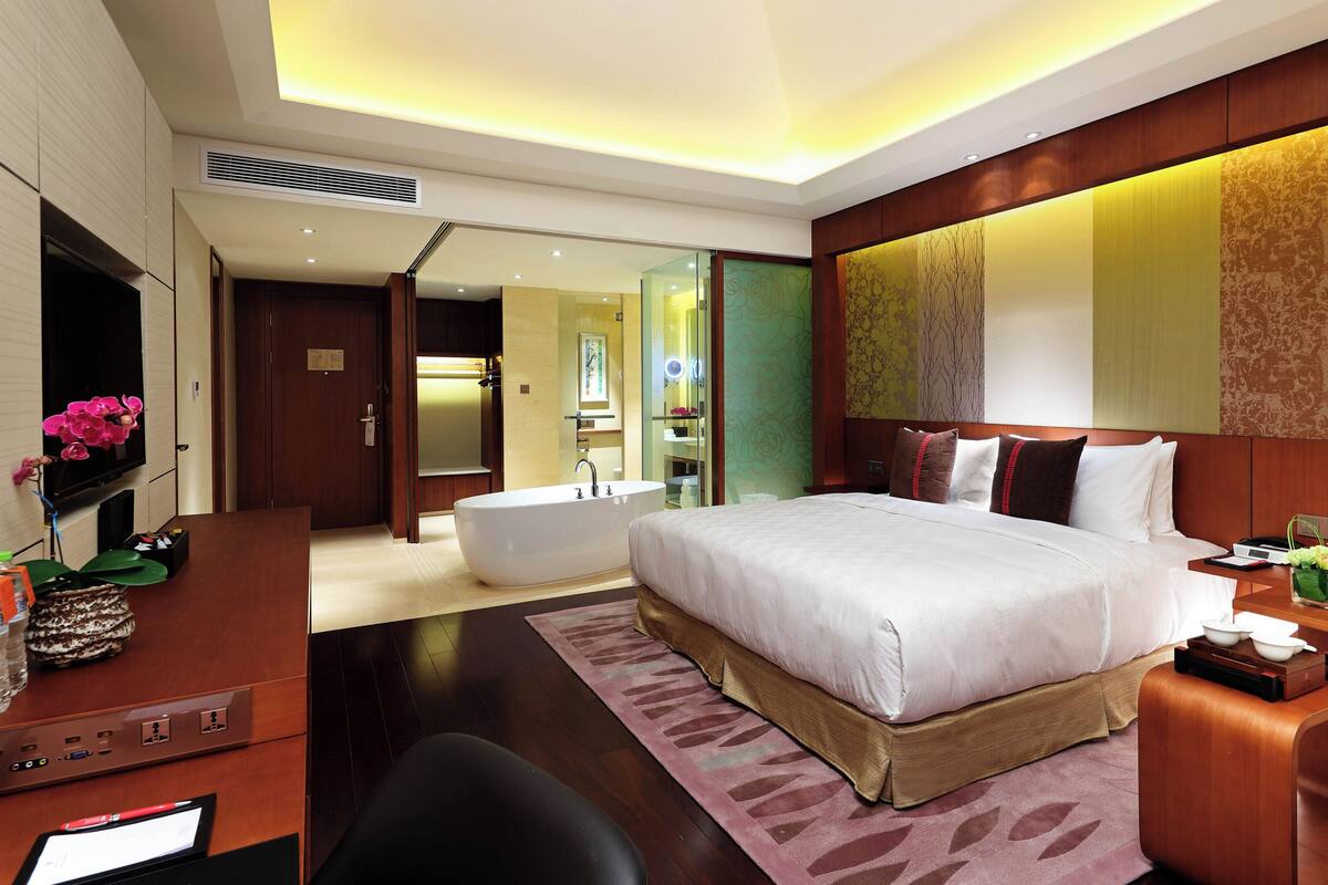 A modern hotel room with a large bed, a separate bathroom, a desk with a computer, and a TV.