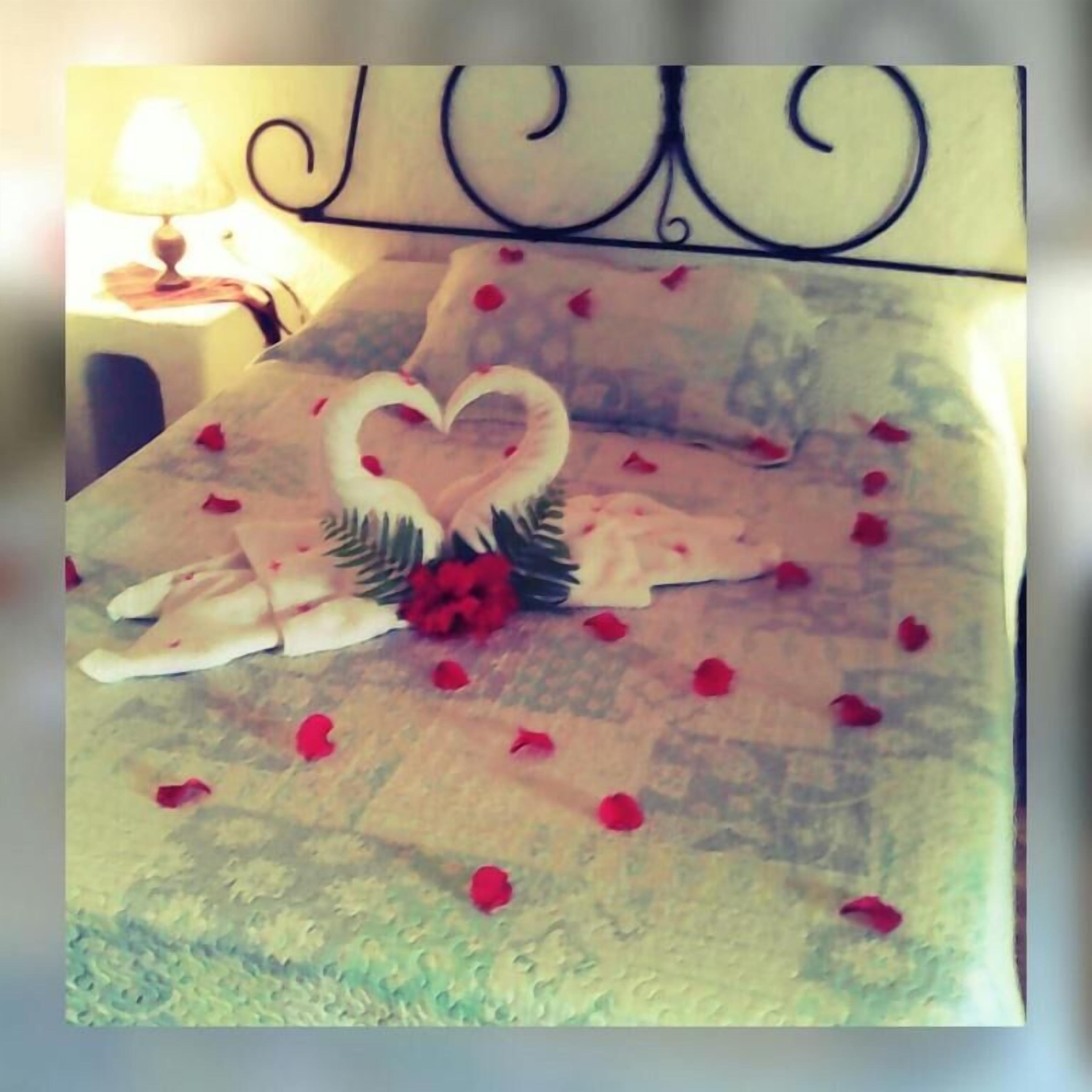 Una cama con pétalos de rosa y un arreglo de plumas con forma de corazón.