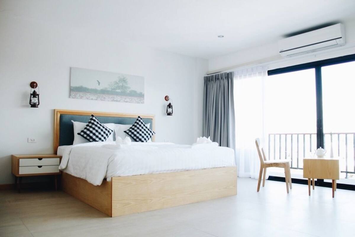 A modern hotel room with a large bed, a bedside table, a chair, and a balcony with a view.