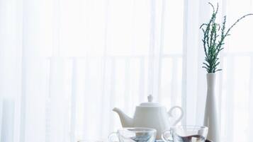 Una tetera blanca y dos tazas de vidrio sobre una bandeja con bolsitas de té y una planta en un florero blanco.