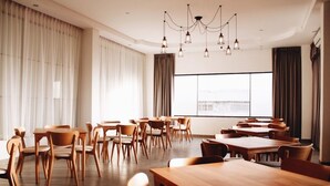 A spacious dining area with wooden tables and chairs, large windows, and a modern chandelier. - Phukaning Hotel (Udon Thani)