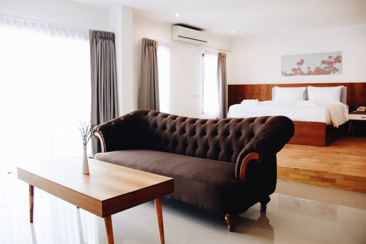 A hotel room with a large bed, a dark brown sofa, a wooden table, and a window with curtains.