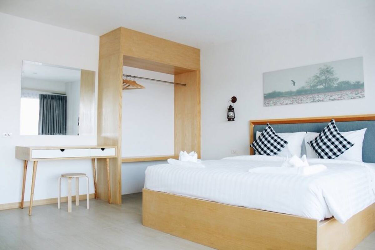 A modern bedroom with a wooden bed frame, white bedding, a bedside table, and a mirror.
