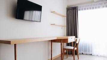 Una habitación minimalista con un escritorio de madera, una silla, un televisor montado y una ventana con cortinas.