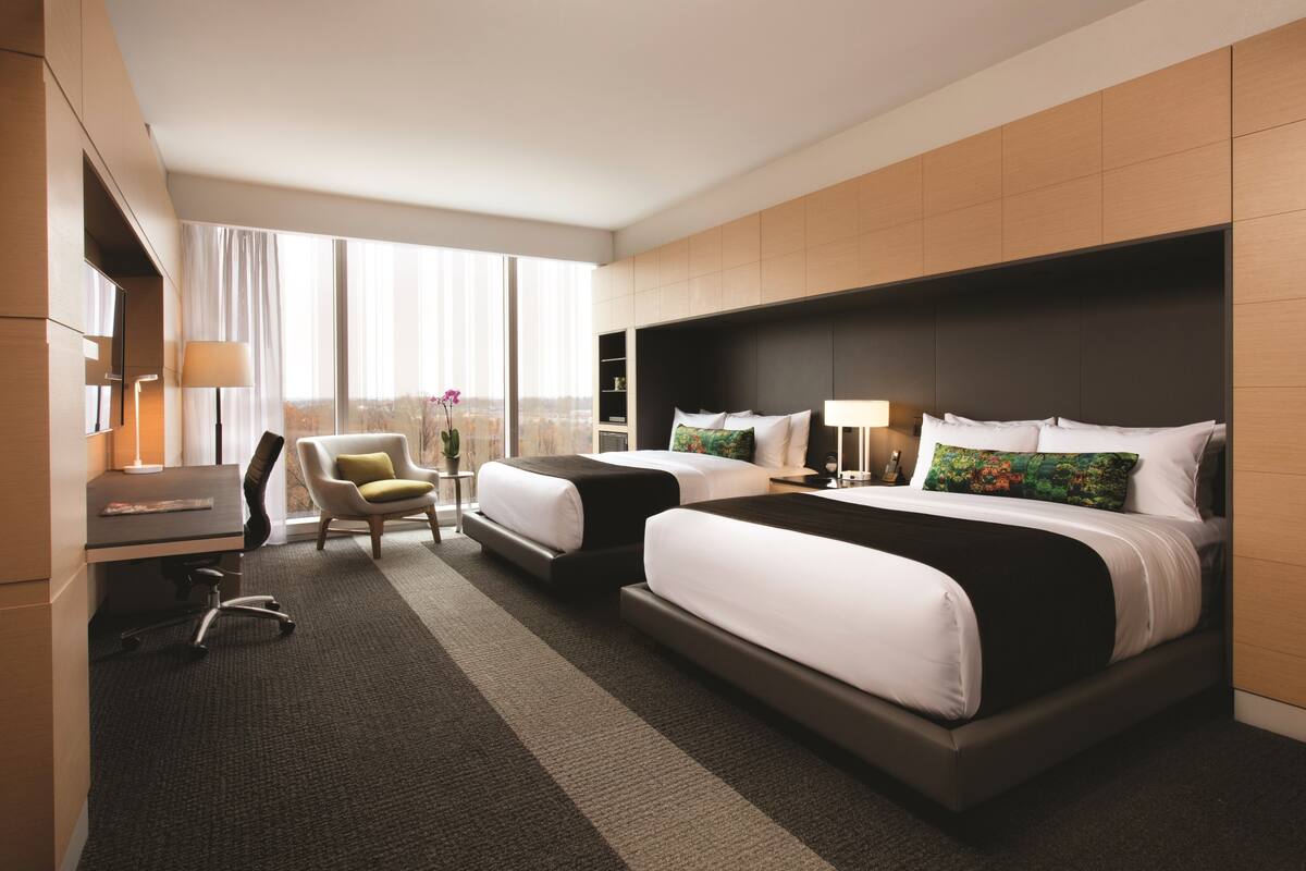 Une chambre d’hôtel avec deux lits, un bureau, une chaise et une grande fenêtre donnant sur la ville.