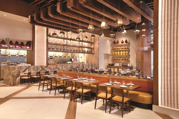 A restaurant with a long counter, multiple tables, and hanging pendant lights.
