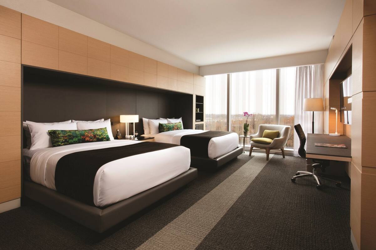 Une chambre d’hôtel avec deux lits, un bureau, une chaise et une grande fenêtre avec des rideaux.