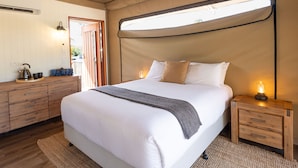 Un dormitorio con una cama grande, mesitas de noche de madera, una pequeña mesa con una tetera y una ventana con una lámpara.