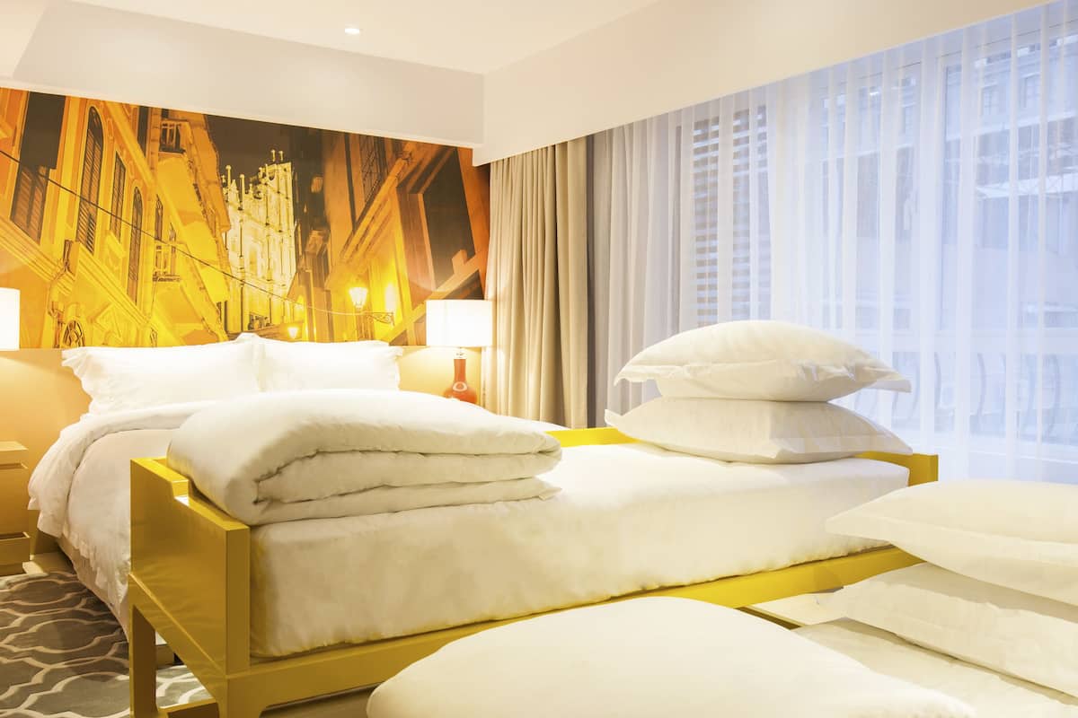 A hotel room with two beds, a large window with curtains, and a mural on the wall.