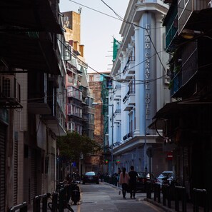 Uma rua estreita ladeada por edifícios altos, incluindo um hotel com uma placa chamativa.