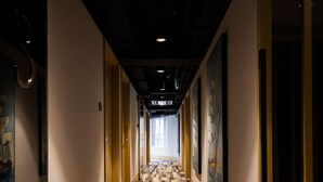 Un couloir d’hôtel avec un tapis à motifs, des œuvres d’art encadrées accrochées aux murs et des portes donnant accès aux chambres.