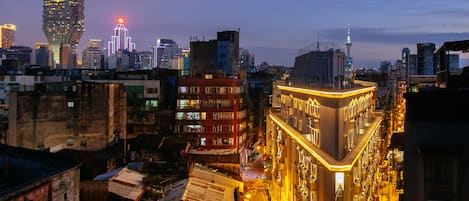 A cityscape at dusk with illuminated buildings, a prominent tower, and a street lined with parked motorcycles.