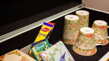 Un depósito de almacenamiento con diversos objetos, incluyendo un paquete de té Lipton, un paquete de té Dilmah y varias tazas con estampado floral.