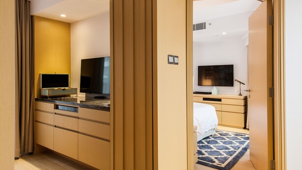 Une chambre d’hôtel moderne avec une cloison en bois, un téléviseur à écran plat, une table de chevet et un tapis à motifs.