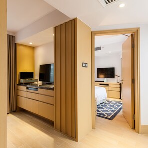 A modern hotel room with a wooden partition, a flat-screen TV, a bedside table, and a patterned rug.